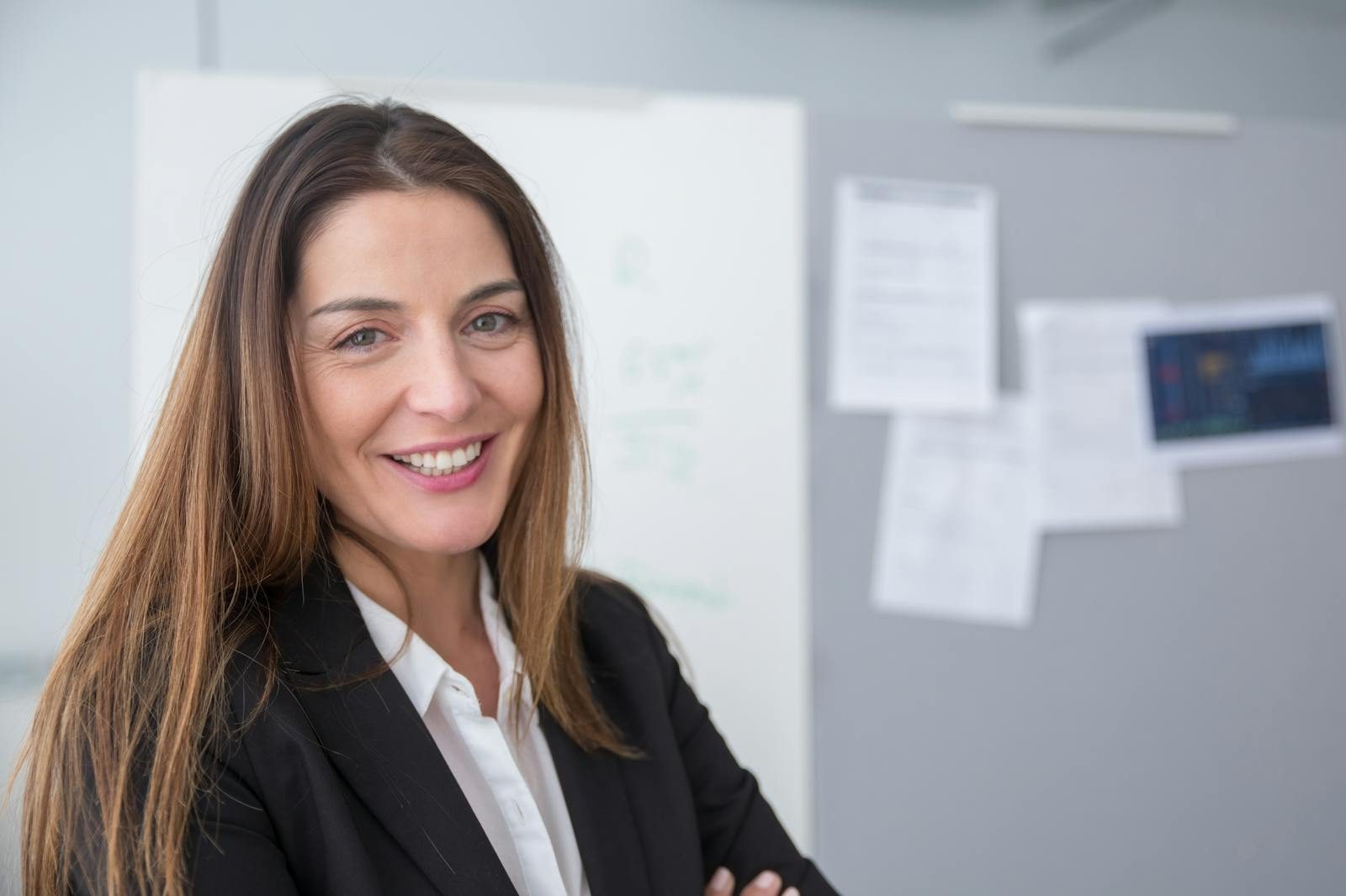 A smiling businesswoman stands confidently in a modern office environment.